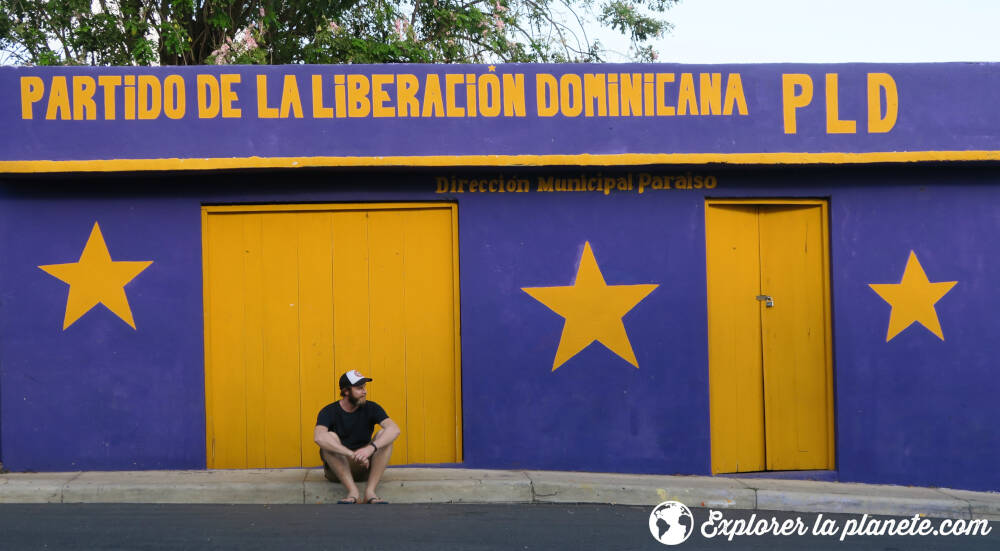 Moi assis devant une maison peinte aux couleurs du partido de la liberacion dominicana