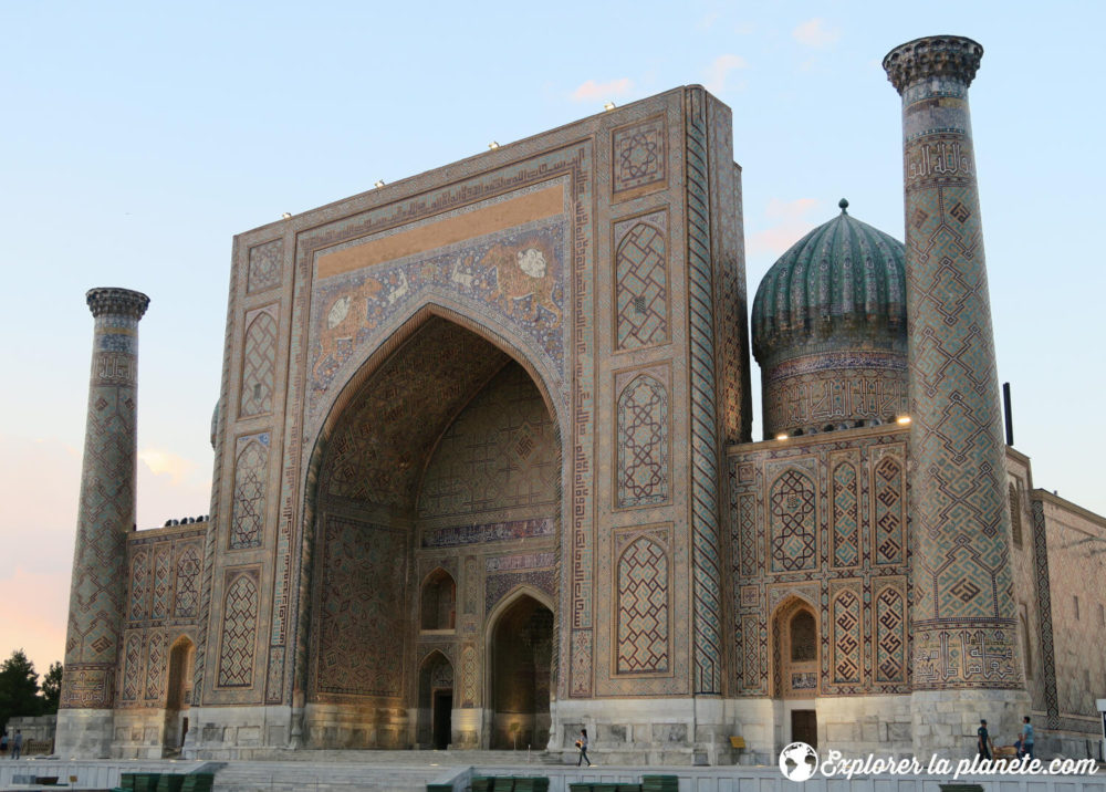 La facade bien détaillée d'une médersa du Régistan à Samarcande. On voit aussi les minarets et un dôme.